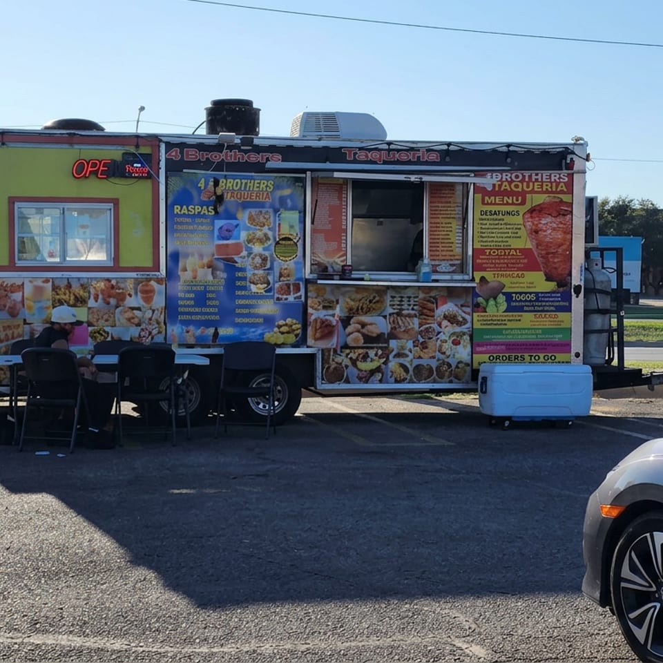 Colorful 4 Brothers Taqueria food truck displaying Mexican dishes, with outdoor tables, customers, and parked vehicles.